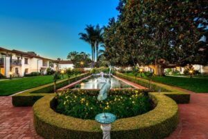 Outdoor garden with a metal crane at the end of a long fountain lined with tropical plants