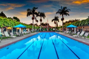 Covenant Living of Samarkand's outdoor in ground swimming pool lined with lounge chairs and palm trees