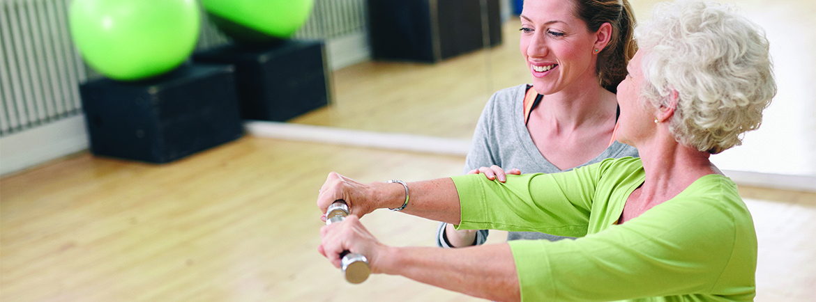 Senior woman assisted by personal trainer in gym